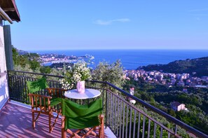 Ein Balkon mit Tisch und Stühlen mit Blick auf eine Küstenstadt und das Meer.