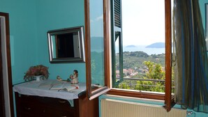 Une pièce avec vue sur un paysage côtier, une fenêtre avec un cadre en bois, une petite table sur laquelle est posé un vase de fleurs, et un radiateur situé sous la fenêtre.