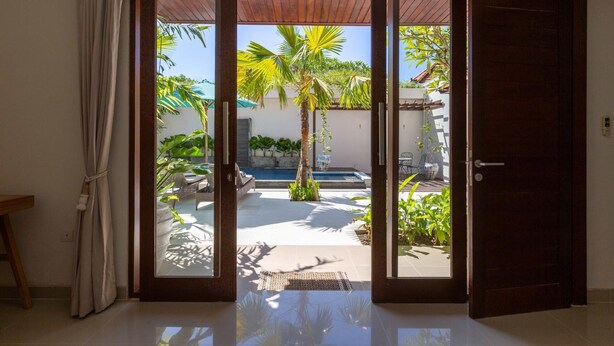 A sliding glass door leading to a pool area with a view of palm trees and a clear sky.