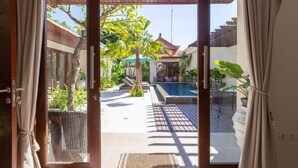 A view through a sliding glass door into a backyard with a swimming pool, lounge chairs, and potted plants.