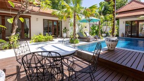 A poolside area with a wooden deck, lounge chairs, and a table with chairs.