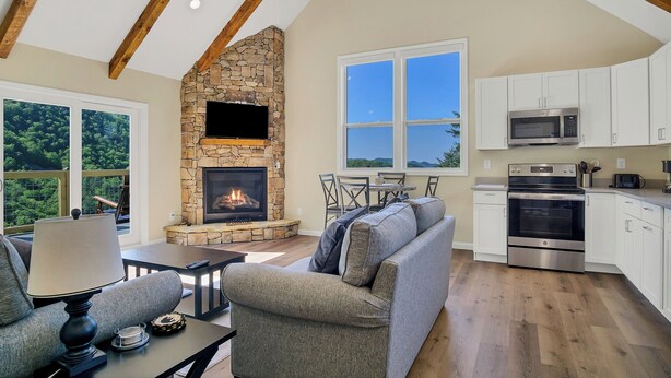 A spacious living room with a stone fireplace, a gray sofa, and a dining area with a table and chairs. - Brand new luxury home with a magnificent view , and luxurious hot-tub (Townsend)
