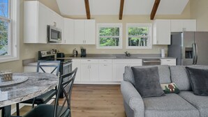 A modern kitchen with white cabinets, a stainless steel refrigerator, and a dining area with a marble table and chairs. - Brand new luxury home with a magnificent view , and luxurious hot-tub (Townsend)