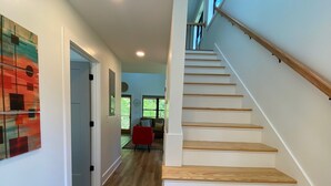 Un intérieur moderne avec un escalier en bois, un fauteuil rouge et une vue sur l’espace de vie.