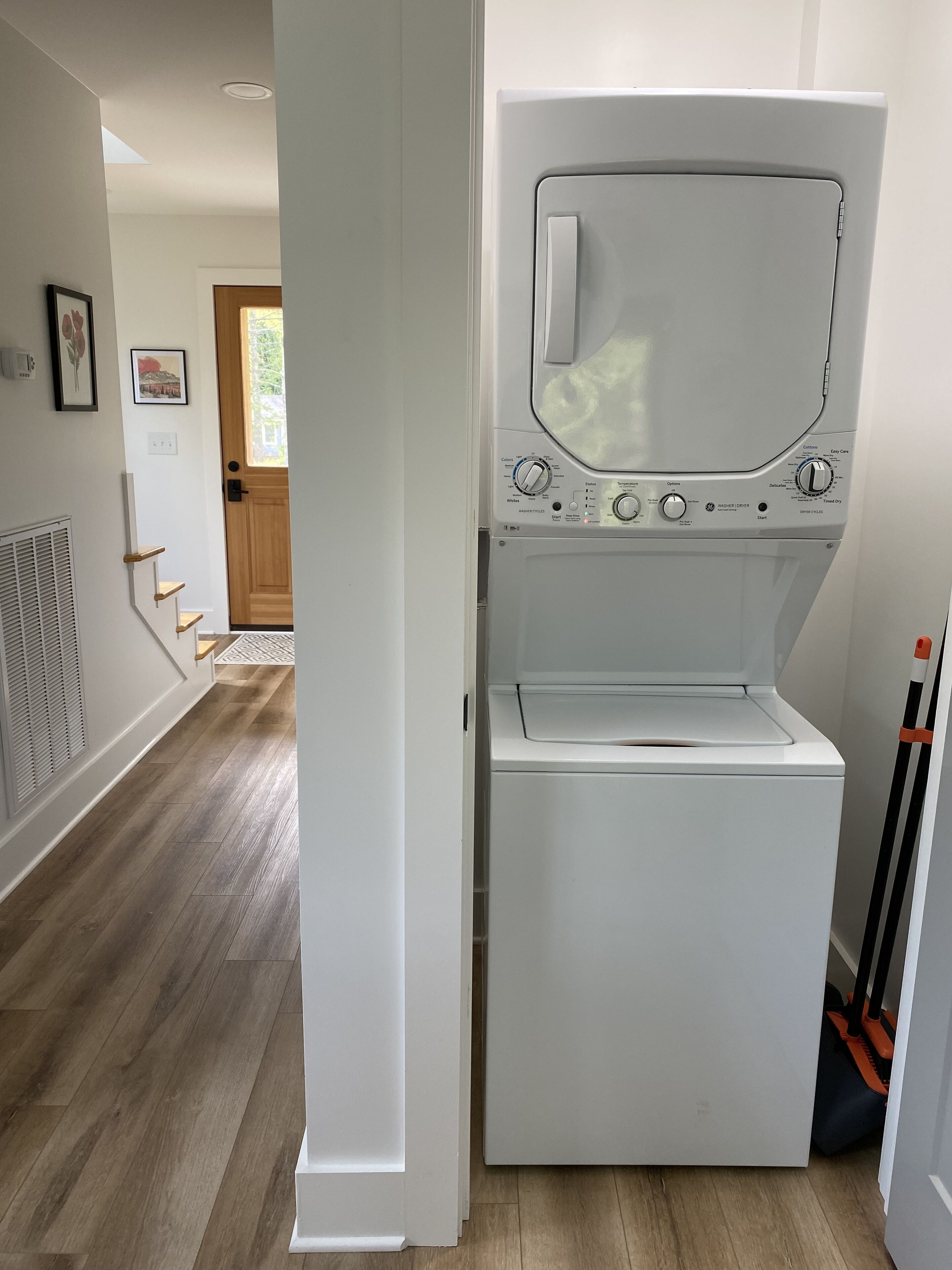 A laundry room with a front-loading washer and dryer, a wooden floor, and a door leading to another room.