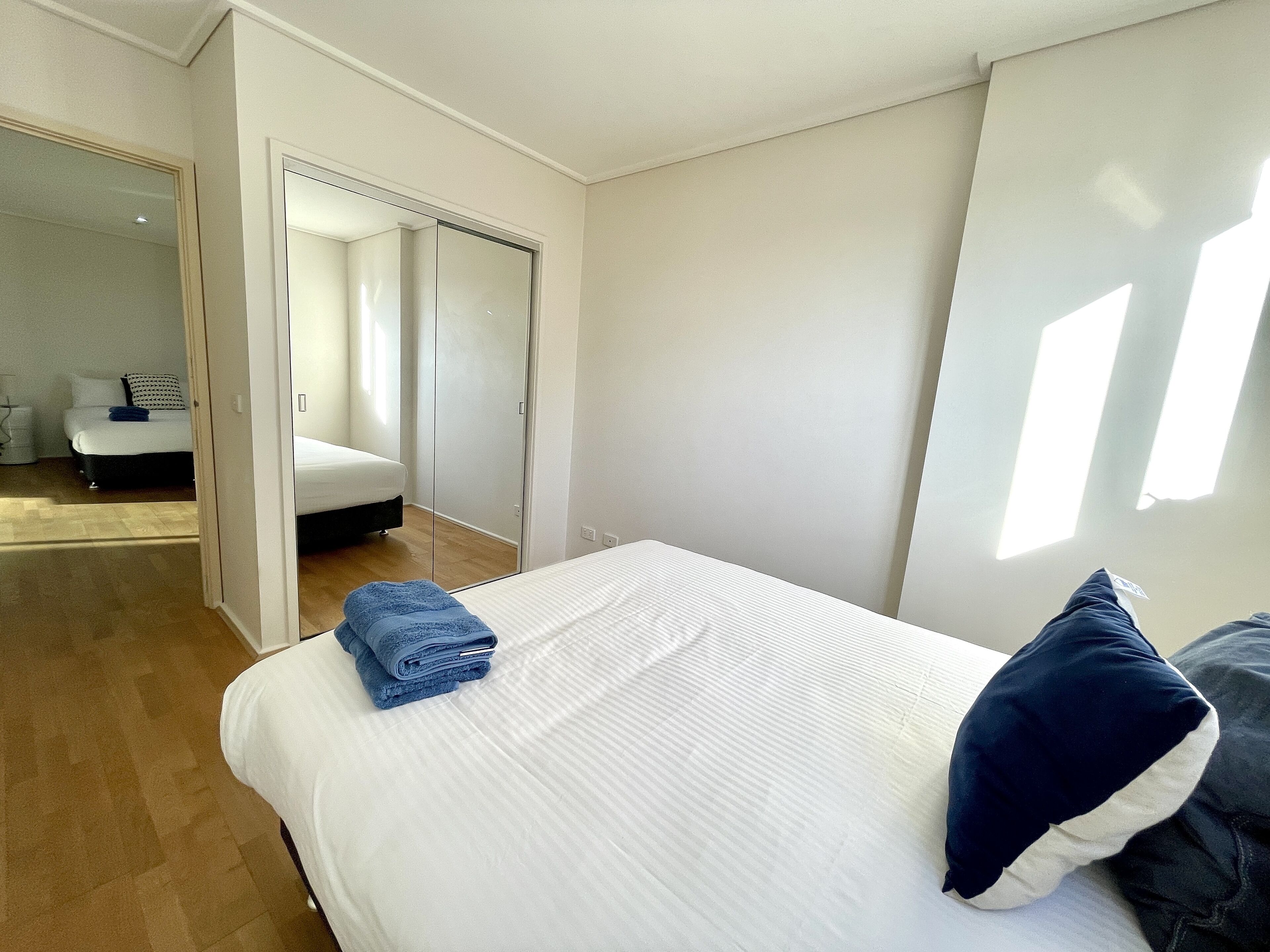 A bedroom with a bed, a blue towel, a dark blue pillow, and a wardrobe.