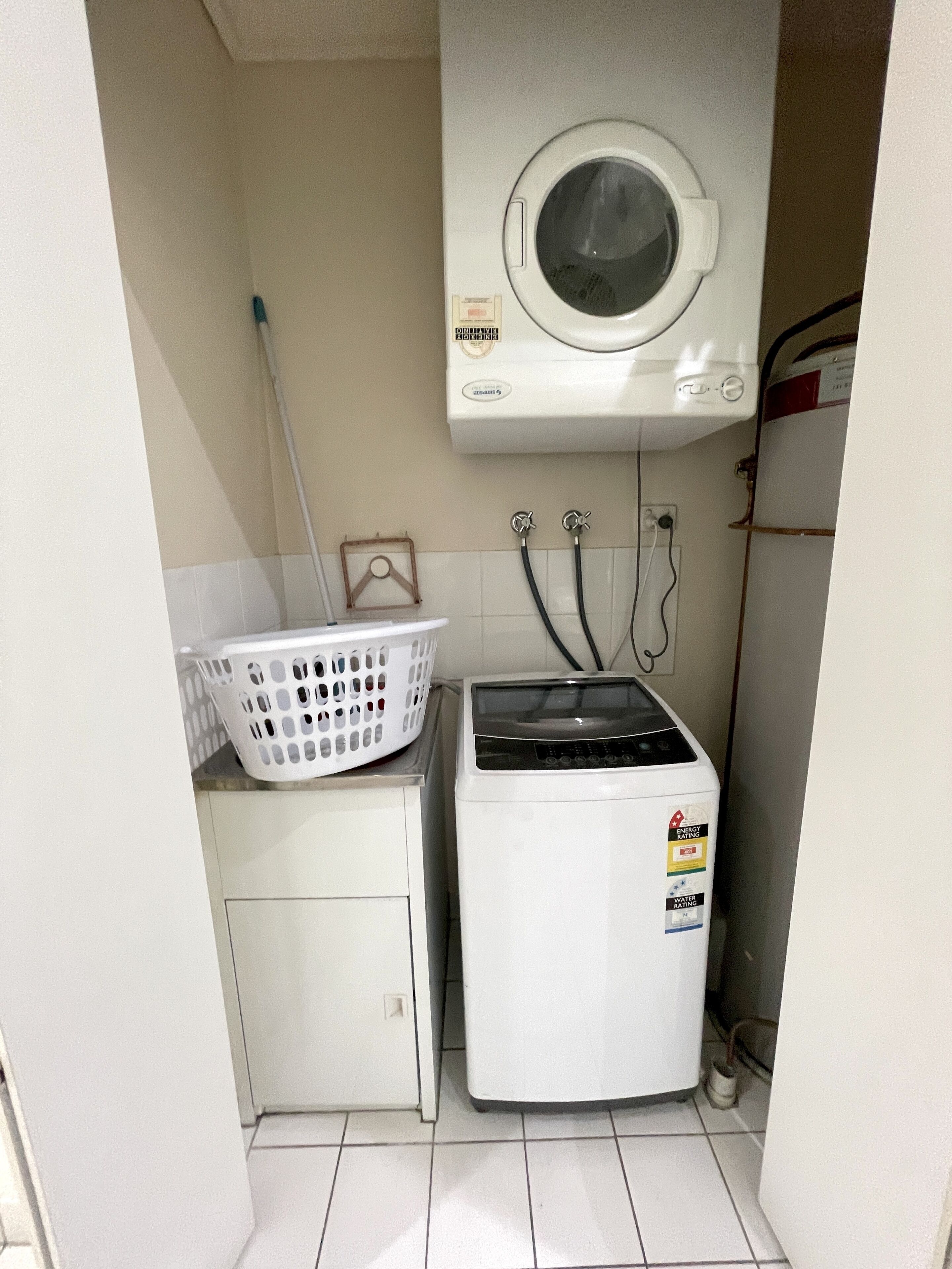 Ein kleiner Waschraum mit Waschmaschine und Trockner, einem Schrank und einem Wäschekorb auf der Ablagefläche.