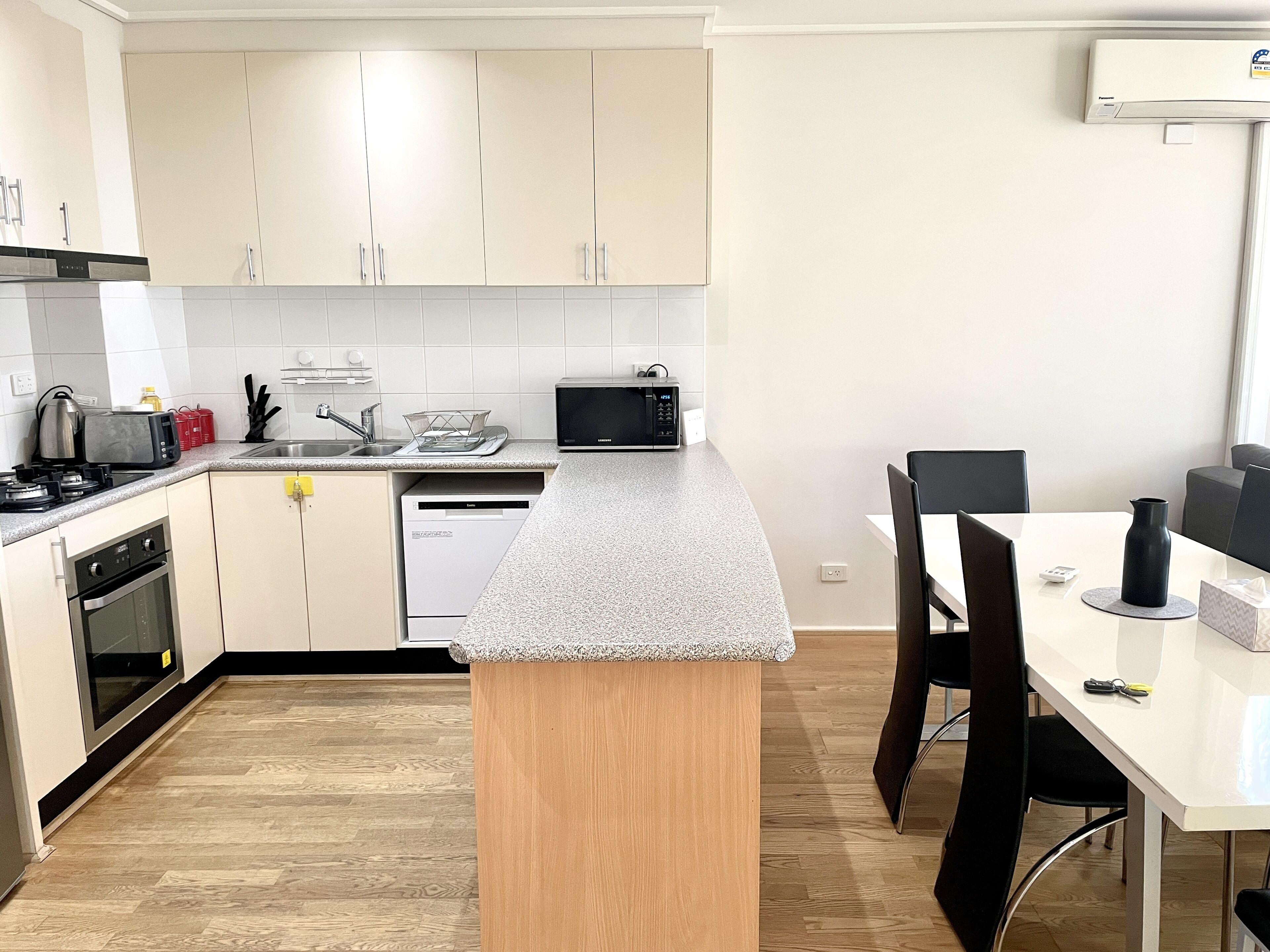 A modern kitchen with white cabinets, a granite countertop, a built-in dishwasher, a microwave, and a dining area with a white table and black chairs.