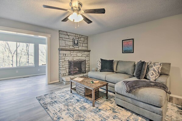 A living room with a stone fireplace, a ceiling fan, a grey sofa, and a coffee table.