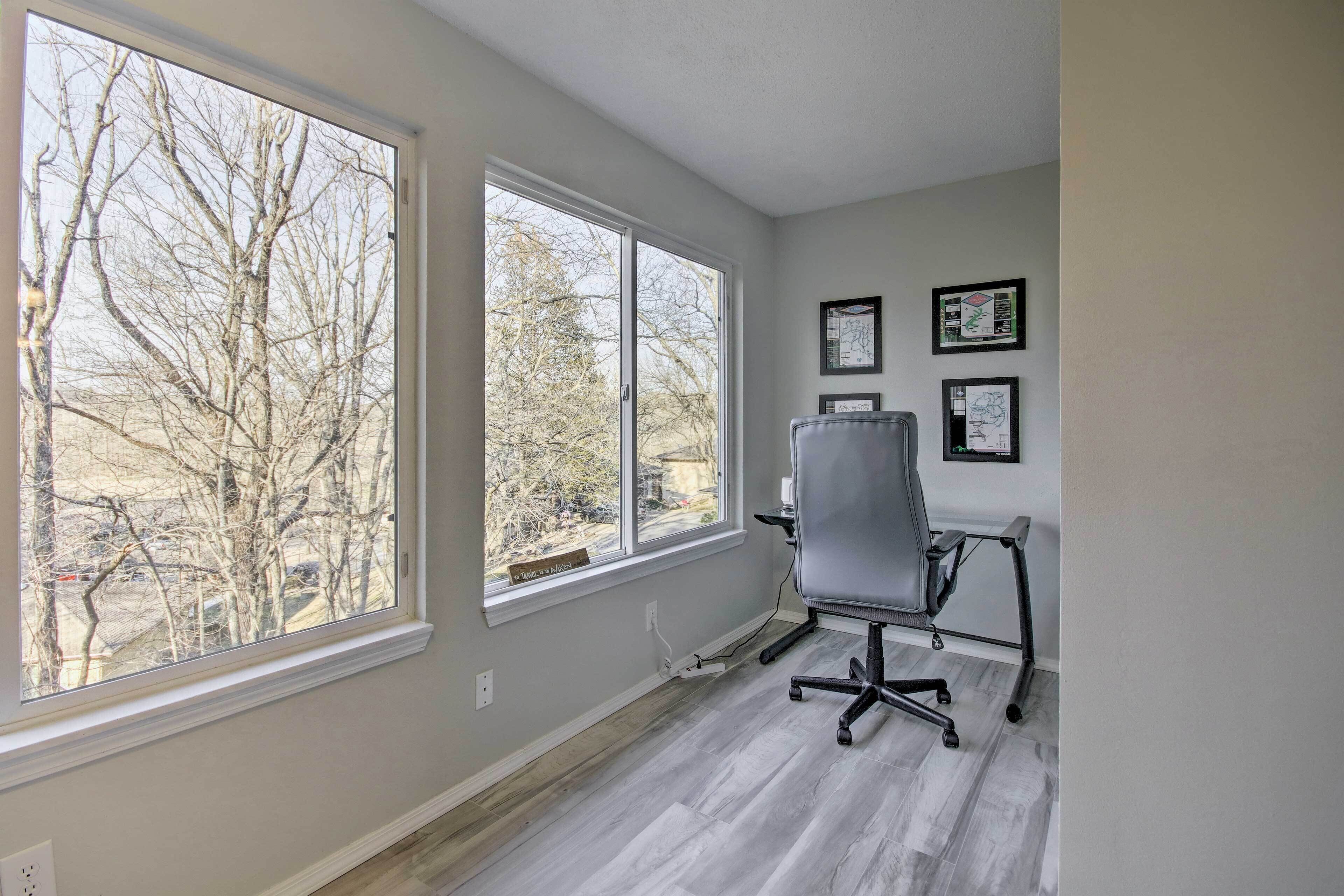 A room with large windows, a gray office chair, and framed artwork on the wall.