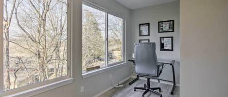 A room with large windows, a gray office chair, and framed artwork on the wall.