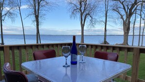 Une table avec deux verres à vin et une bouteille, placée sur une terrasse donnant sur une étendue d’eau.