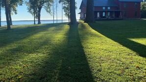 A grassy area with a large tree and a red building with a blue roof. - Red House Lodge (Champlain)