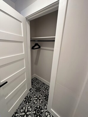 Ein begehbarer Kleiderschrank mit einem gemusterten Boden, einer Kleiderstange und einer Tür mit horizontalen Füllungen.