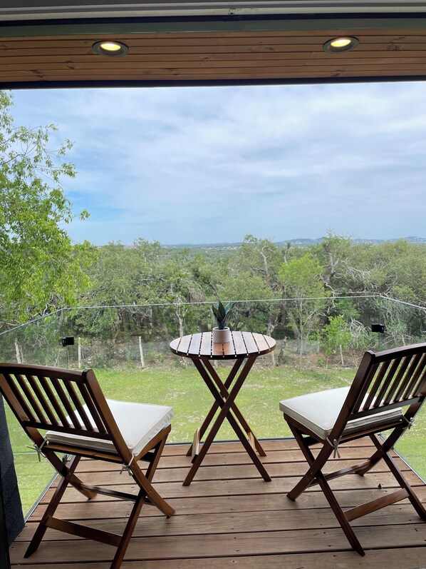 An outdoor deck with two wooden chairs and a small round table, overlooking a lush landscape.