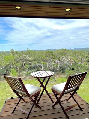 A wooden deck with two chairs and a small table, overlooking a lush landscape with trees and hills.