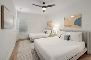 A bedroom with two beds, a ceiling fan, and abstract wall art.