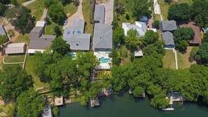 An aerial view of a residential area with houses, a swimming pool, and a dock extending into a body of water.