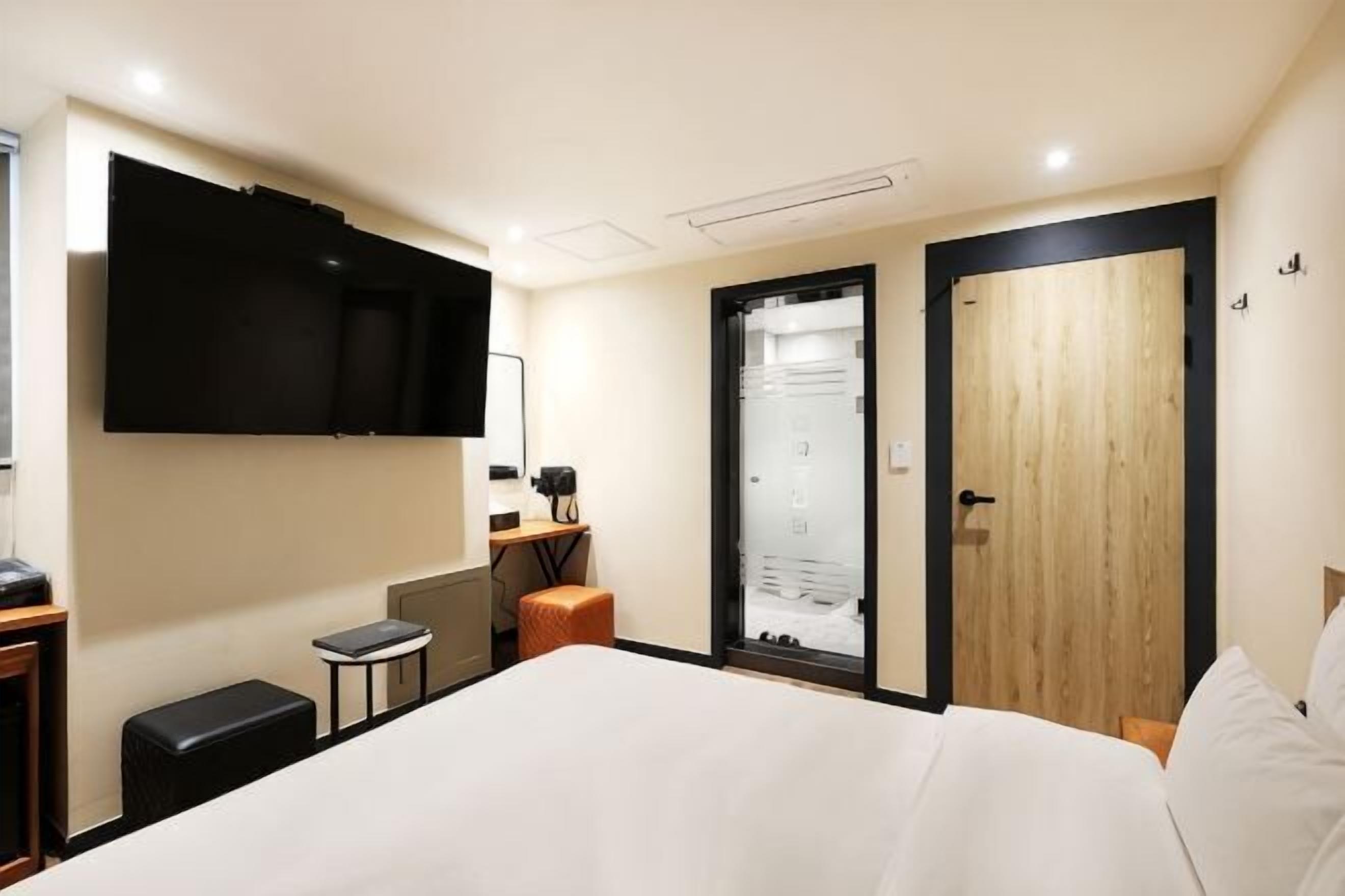 Een hotelkamer met een bed, een bureau met een computer, een aan de muur bevestigde televisie en een houten deur.