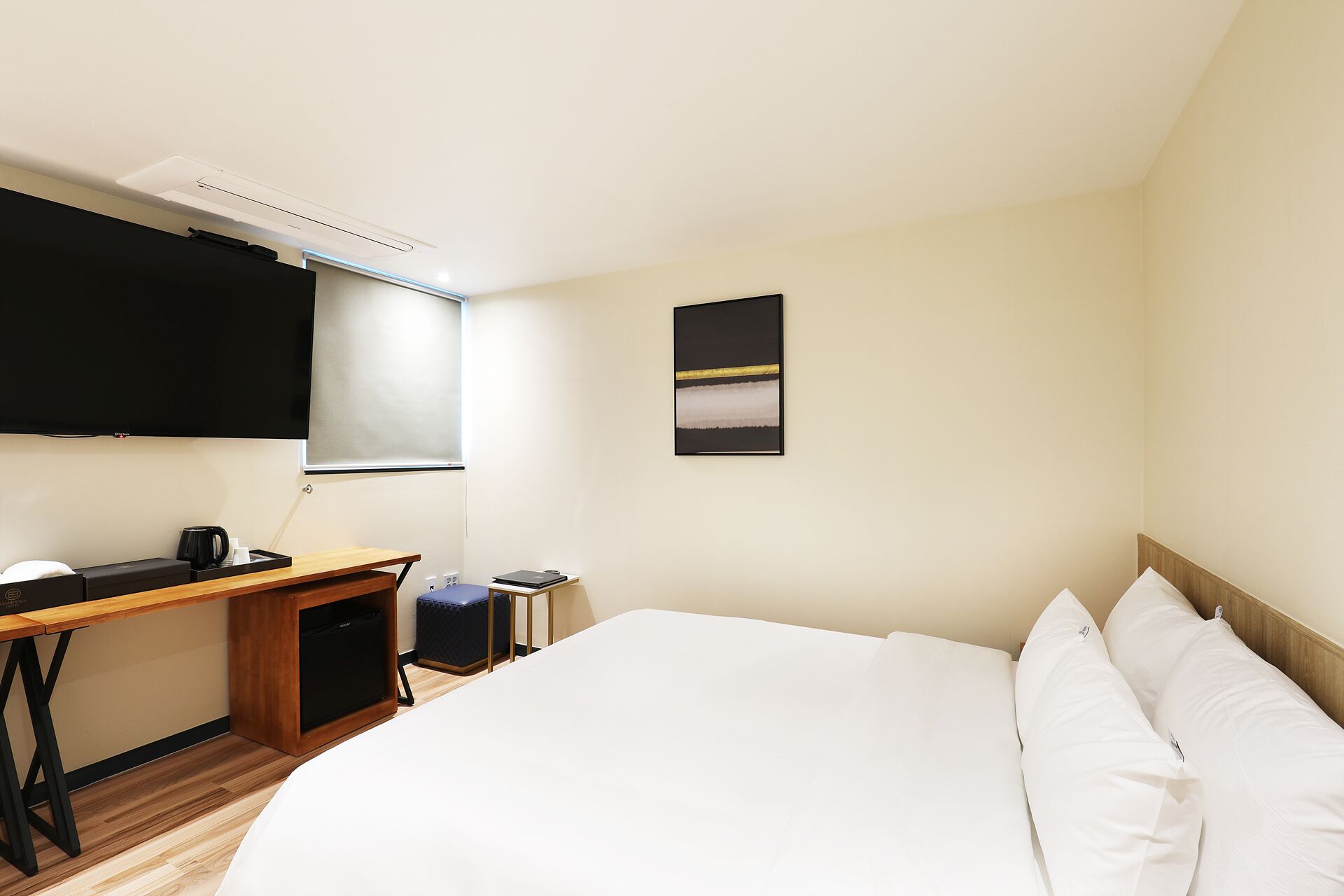 Habitación de hotel con cama, escritorio, silla, televisión y una pequeña mesa con cafetera.
