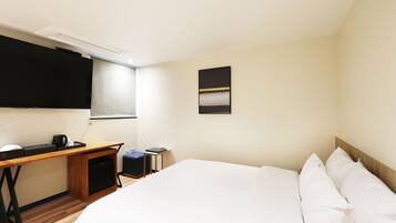 Habitación de hotel con cama, escritorio, silla, televisión y una pequeña mesa con cafetera.