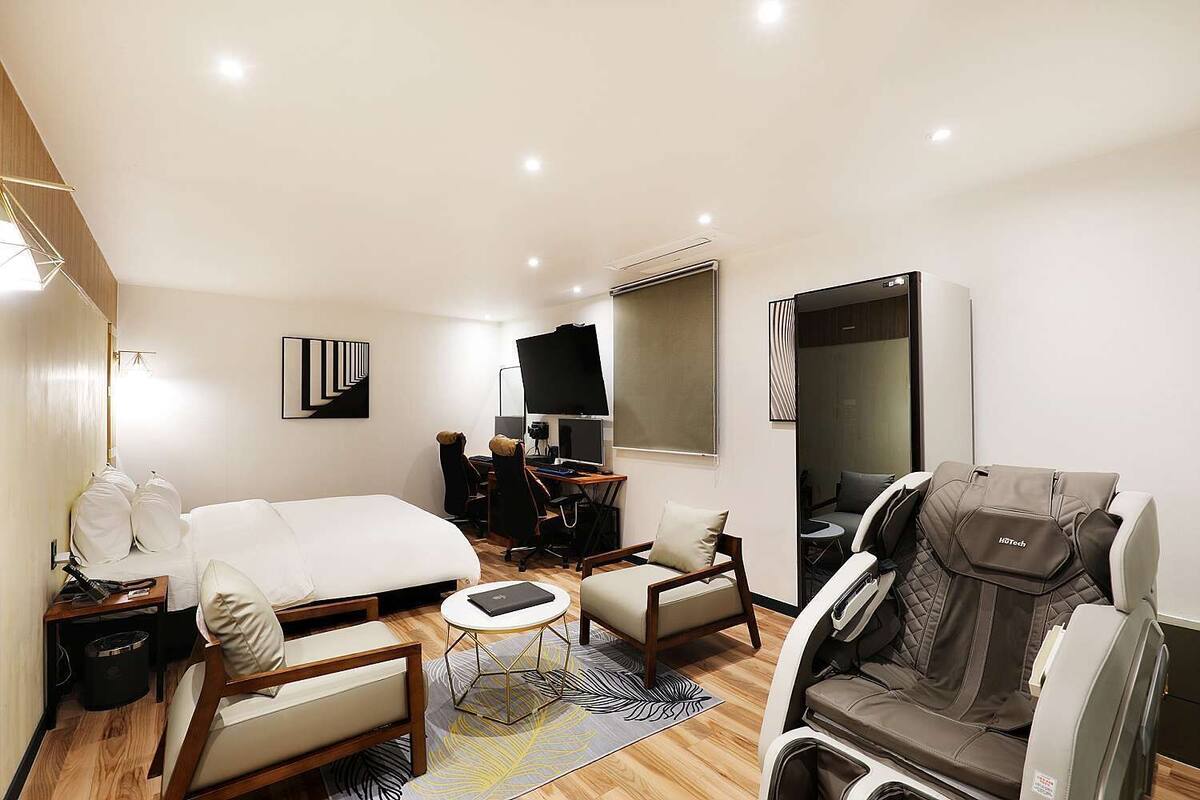 Ein Hotelzimmer mit einem Bett, einem Schreibtisch mit Computer, einem Sessel und einem Massagesessel sowie einem Fernseher.