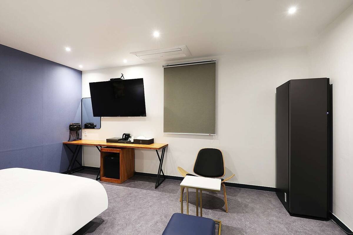 Ein Hotelzimmer mit Bett, Schreibtisch, Stuhl, Fernseher und Kleiderschrank.
