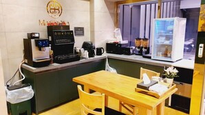 Eine kleine, moderne Küchenzeile mit einer Kaffeemaschine, einem Kühlschrank und einem Fenster mit Jalousien.