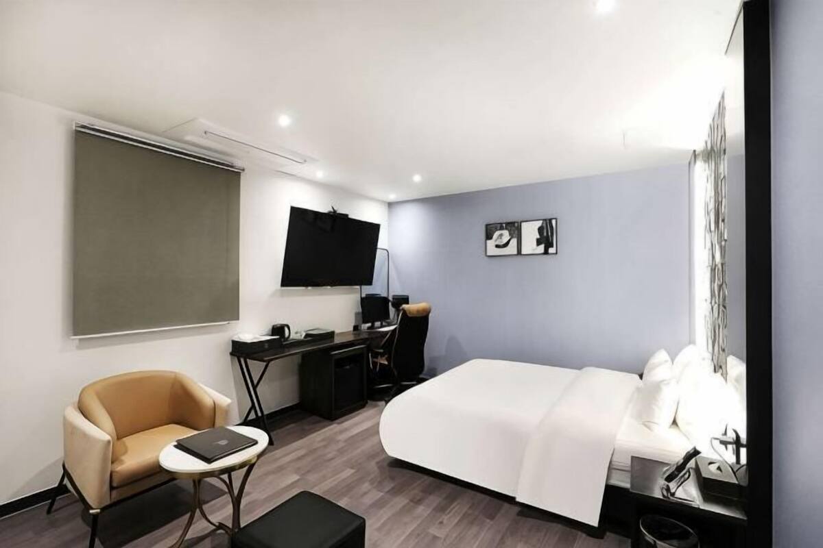 Ein Hotelzimmer mit einem Bett, einem Schreibtisch mit Computer, einem Stuhl, einem Fernseher und einem Fenster.