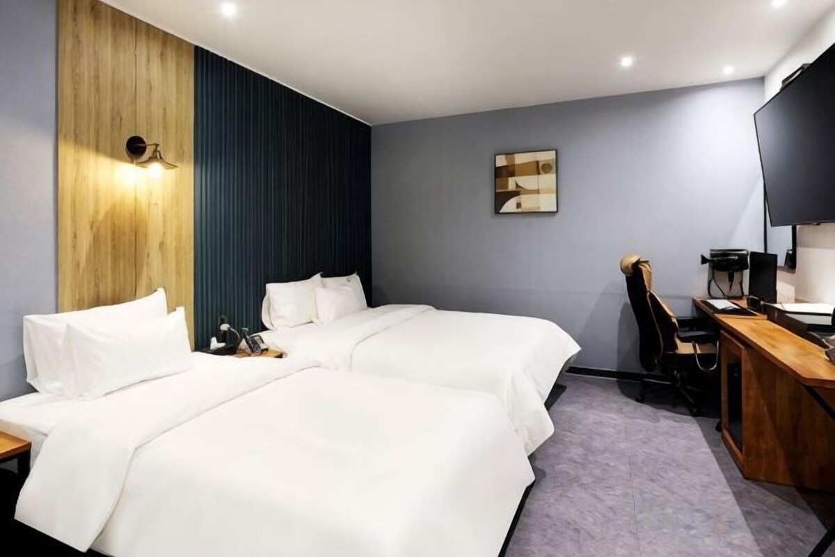 Une chambre d’hôtel avec deux lits, un bureau, une chaise et un téléviseur.
