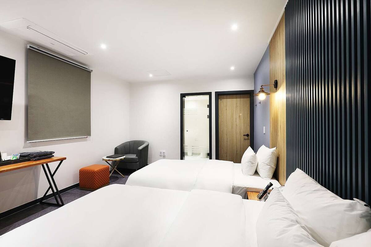 Ein modernes Hotelzimmer mit zwei Betten, einem Schreibtisch, einem Stuhl und einem großen Fenster.