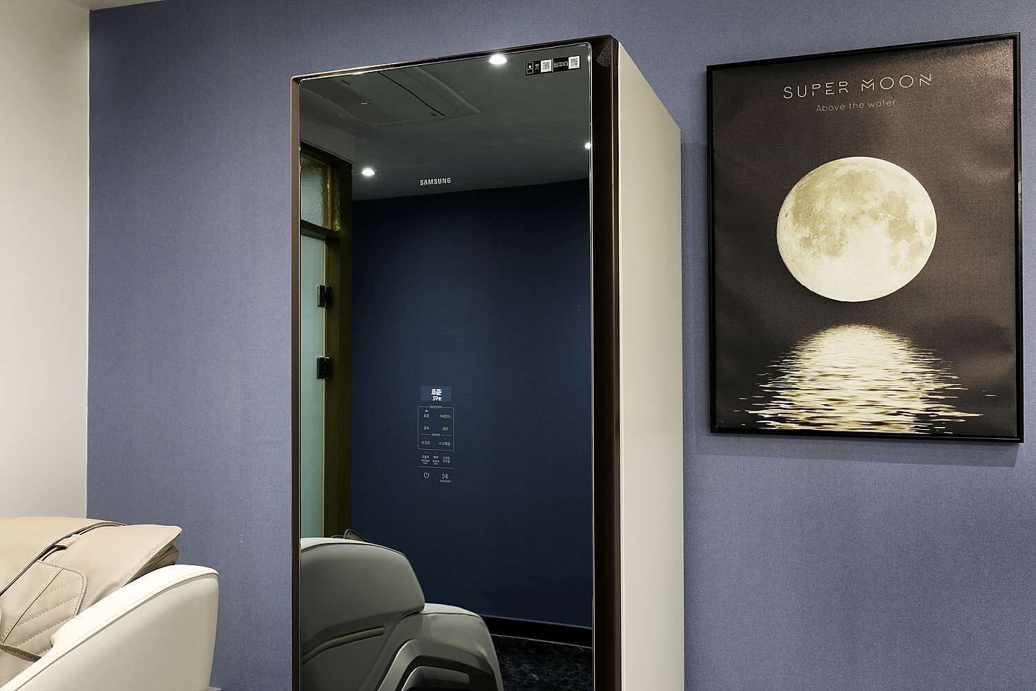 A hotel room with a large window, a wall-mounted artwork of the moon, and a Samsung refrigerator.