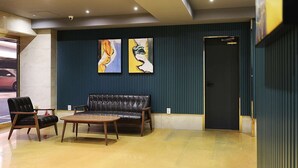 Eine Lobby mit Ledersofa, zwei Sesseln, einem Holztisch und zwei abstrakten Gemälden an der Wand.
