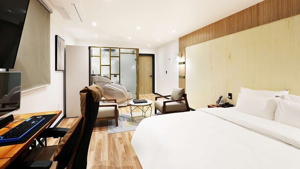 Ein modernes Hotelzimmer mit einem großen Bett, einem Schreibtisch mit Computer, einem Sessel, einem kleinen Tisch und einem Fernseher.
