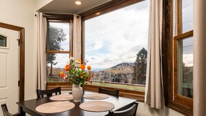 Ein Esstisch mit vier Stühlen, eine Vase mit Blumen und Blick auf eine Landschaft durch große Fenster.