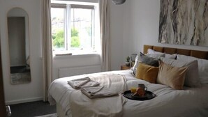 Ein ordentlich bezogenes Bett mit einem Frühstücksbrett, ein Nachttisch mit Lampe und ein großes abstraktes Gemälde an der Wand.