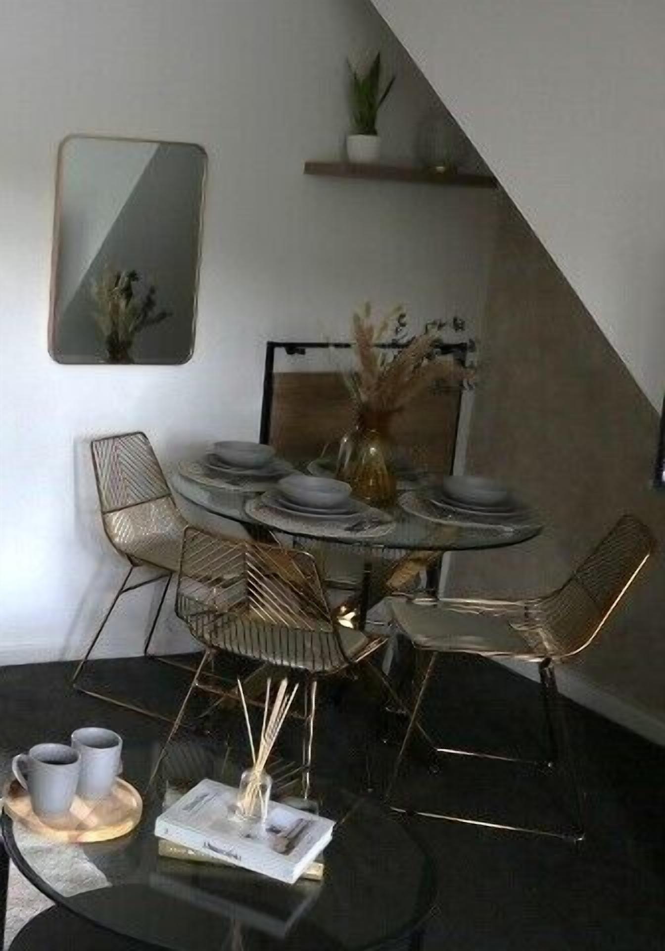 Een eetruimte met een ronde tafel, vier stoelen en een bijzettafeltje met kopjes en een boek.