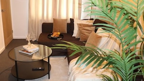 Ein Wohnzimmer mit einer Couch, einem Glastisch und einer Topfpflanze.