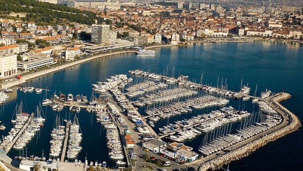 An aerial view of a marina with numerous boats docked, surrounded by a cityscape with buildings and mountains in the background. - Cool attic apt w gallery, in the heart of Split (Split)