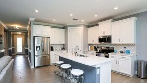 Una cocina moderna con gabinetes blancos, electrodomésticos de acero inoxidable y una isla central con taburetes de bar.