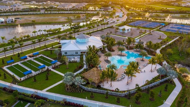 Vista aérea de un complejo turístico con una piscina central, varias canchas de tenis y una casa grande con techo azul.