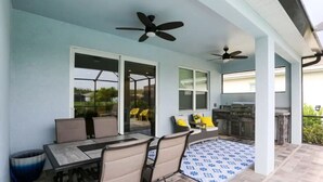 Un patio al aire libre con una mesa de comedor, sillas, ventiladores de techo y una parrilla.