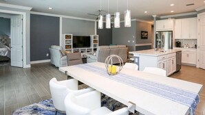 Una cocina moderna con armarios blancos, una isla central y un comedor con una mesa larga y sillas blancas.