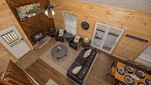 L’intérieur d’un chalet en bois comprend une cheminée, un canapé en cuir, une table à manger et un ventilateur de plafond.