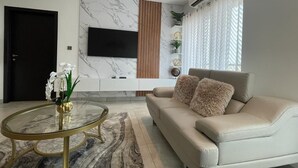 Un salon moderne avec un canapé beige, une table basse ronde en verre, un téléviseur à écran plat fixé au mur et un élément décoratif mural.