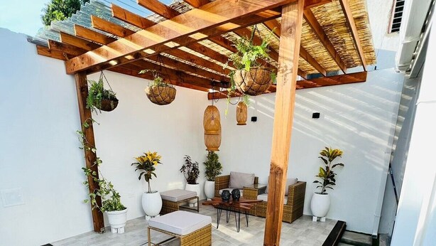 A covered patio area with a wooden pergola, wicker furniture, potted plants, and a small table. - Hermosa Y Divertida Casa, Cerca A LA Playa Y AL Centro Histórico (Santa Marta)