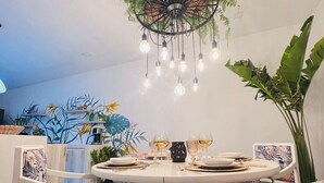 A round dining table with white plates, glasses, and cutlery, surrounded by chairs with patterned cushions. A unique chandelier with hanging bulbs and a decorative base is above the table. - Hermosa Y Divertida Casa, Cerca A LA Playa Y AL Centro Histórico (Santa Marta)