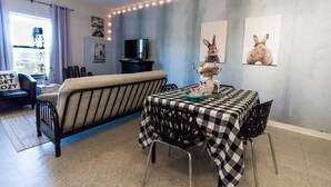Una sala de estar acogedora con un sofá, una mesa de comedor con mantel a cuadros y un televisor sobre un mueble.