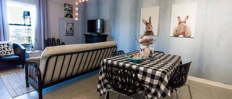 A cozy living room with a sofa, a dining table with a checkered tablecloth, and a TV on a stand.