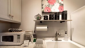 Una cocina con microondas, cafetera y pileta. Hay platos y una botella de lavavajillas en la mesada.